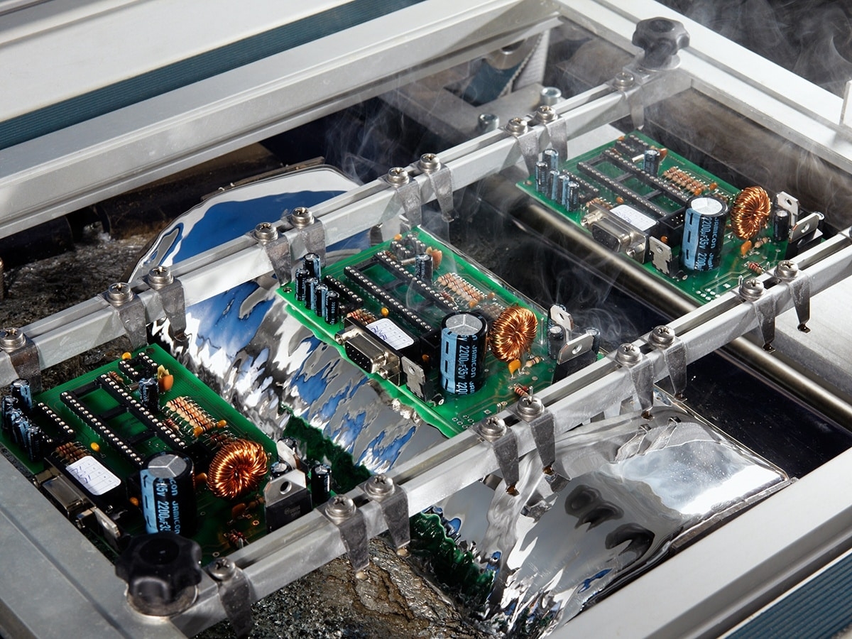 Through-hole PCB passing over solder wave with visible fountain and flux application