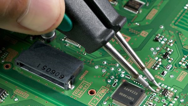 Hand placing a small SMT component on a PCB using tweezers